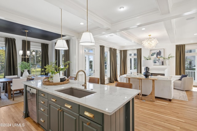 kitchen with sink, light stone counters, decorative light fixtures, a chandelier, and an island with sink