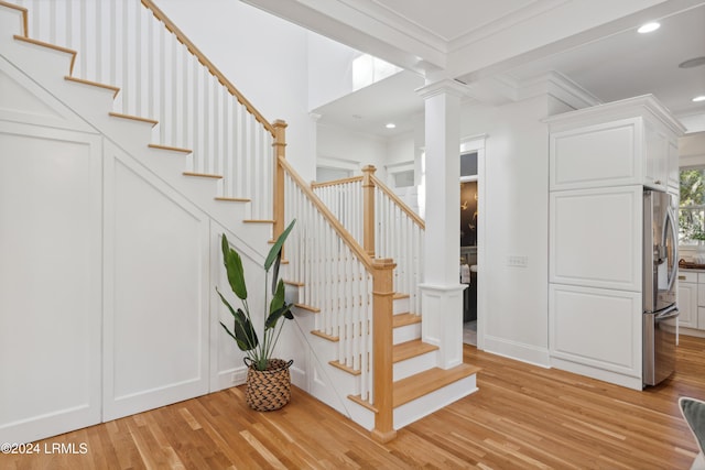 staircase featuring decorative columns, wood-type flooring, and ornamental molding