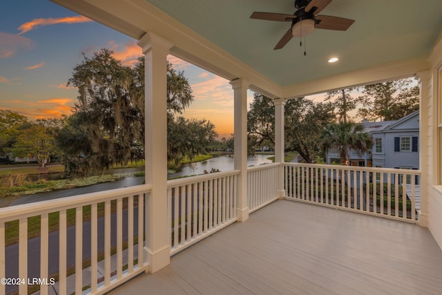 deck at dusk with a water view, ceiling fan, and covered porch