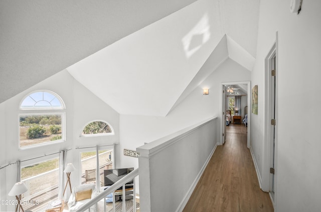 corridor featuring high vaulted ceiling, baseboards, an upstairs landing, and wood finished floors