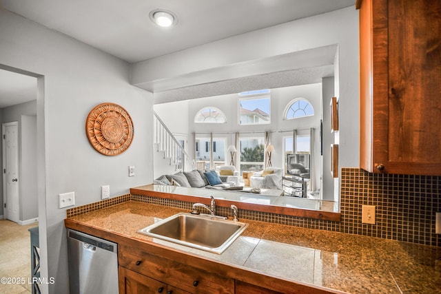 kitchen featuring tasteful backsplash, brown cabinetry, open floor plan, a sink, and stainless steel dishwasher