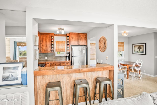 kitchen featuring tasteful backsplash, brown cabinets, freestanding refrigerator, a peninsula, and open shelves