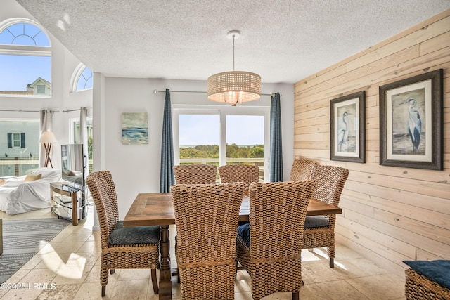 dining area featuring a chandelier, a healthy amount of sunlight, wooden walls, and a textured ceiling