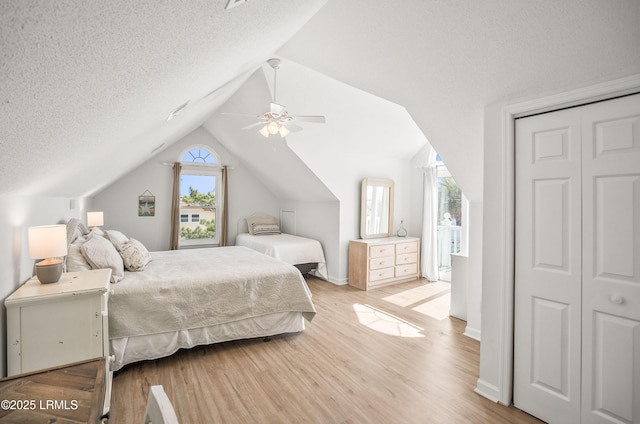 bedroom featuring light wood finished floors, lofted ceiling, a ceiling fan, a textured ceiling, and baseboards