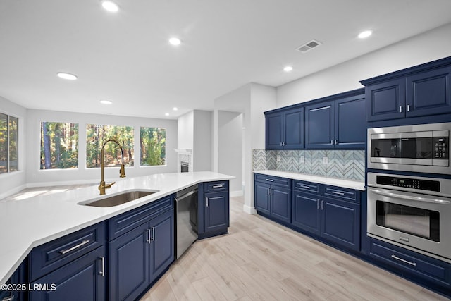 kitchen featuring blue cabinets, sink, light wood-type flooring, appliances with stainless steel finishes, and backsplash