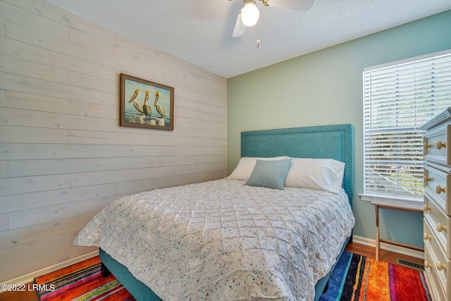 bedroom with hardwood / wood-style flooring, ceiling fan, a textured ceiling, and wood walls