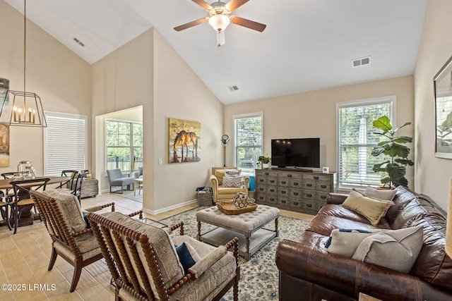 living area featuring a wealth of natural light, ceiling fan with notable chandelier, and visible vents