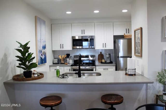 kitchen with tasteful backsplash, white cabinetry, a kitchen bar, kitchen peninsula, and stainless steel appliances