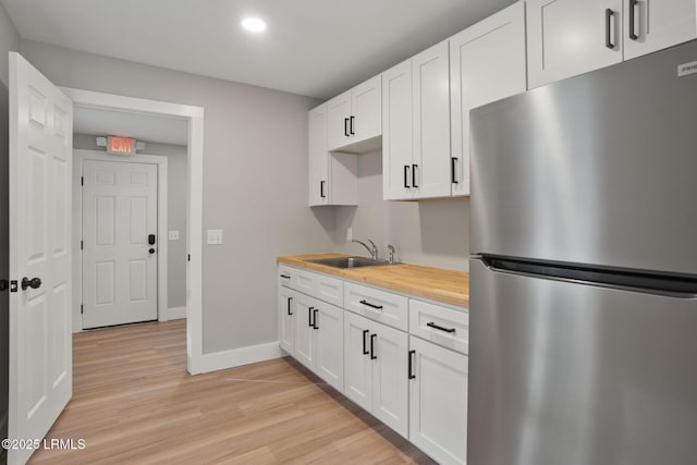 kitchen with a sink, freestanding refrigerator, light wood-type flooring, baseboards, and wood counters