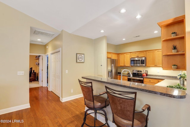 kitchen with appliances with stainless steel finishes, dark stone countertops, a kitchen bar, light hardwood / wood-style floors, and kitchen peninsula