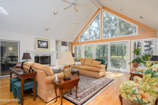 living room with plenty of natural light, high vaulted ceiling, a fireplace, built in shelves, and light wood-type flooring