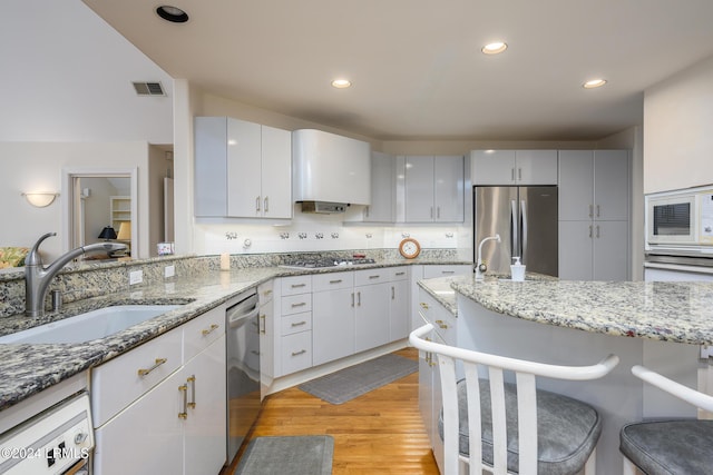 kitchen featuring sink, light hardwood / wood-style flooring, appliances with stainless steel finishes, white cabinetry, and light stone counters