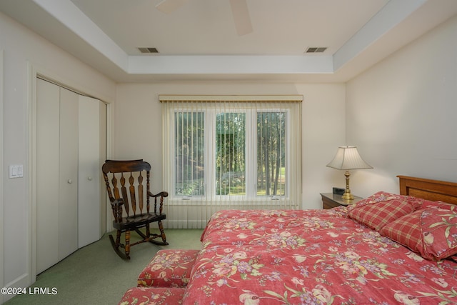 bedroom featuring a tray ceiling, light carpet, ceiling fan, and a closet