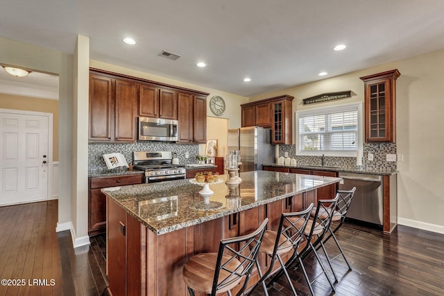 kitchen with visible vents, a sink, a center island, stainless steel appliances, and glass insert cabinets