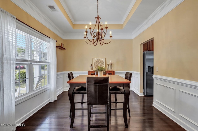 dining space with visible vents, a wainscoted wall, dark wood-type flooring, a notable chandelier, and a tray ceiling