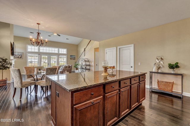 kitchen featuring a notable chandelier, dark stone countertops, a kitchen island, dark wood-style floors, and baseboards