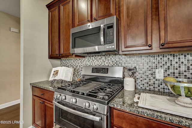 kitchen with dark wood-type flooring, dark stone countertops, appliances with stainless steel finishes, decorative backsplash, and baseboards