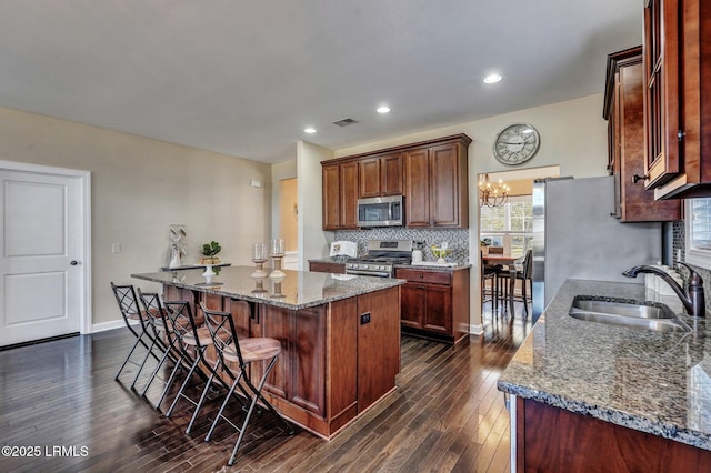 kitchen featuring visible vents, a kitchen island, a sink, appliances with stainless steel finishes, and backsplash