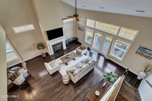 living room with a ceiling fan, wood finished floors, baseboards, high vaulted ceiling, and a fireplace with flush hearth