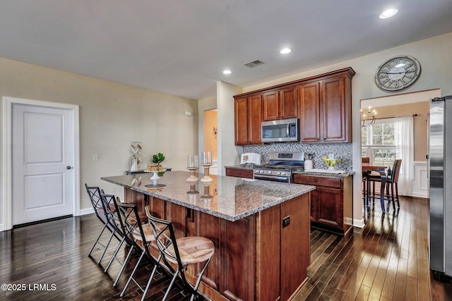 kitchen featuring visible vents, light stone counters, a kitchen island, appliances with stainless steel finishes, and dark wood-style flooring