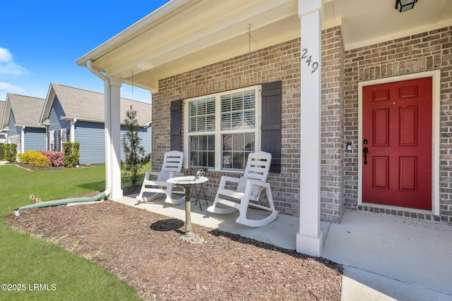 property entrance with brick siding, covered porch, and a yard