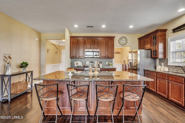 kitchen with visible vents, a kitchen island, light stone counters, stainless steel appliances, and a sink