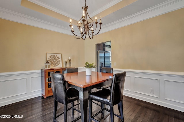 dining area featuring dark wood finished floors, an inviting chandelier, a wainscoted wall, and a tray ceiling