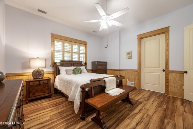 bedroom with a ceiling fan, wainscoting, visible vents, and light wood-style flooring