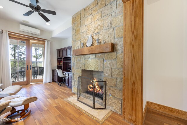 living area with a stone fireplace, baseboards, french doors, light wood finished floors, and a wall mounted air conditioner