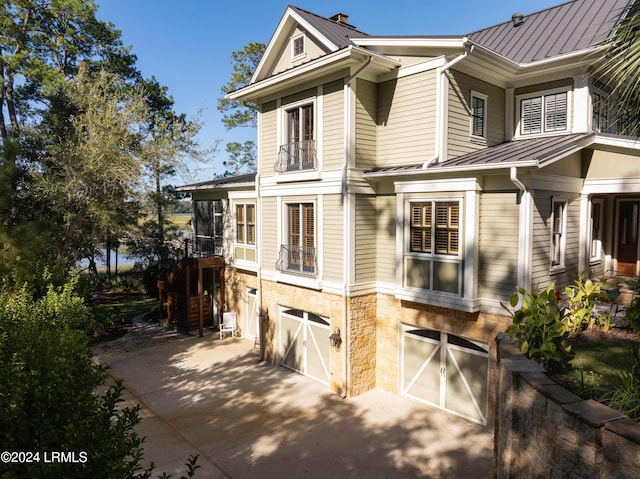 view of property exterior featuring driveway, a standing seam roof, stone siding, and metal roof