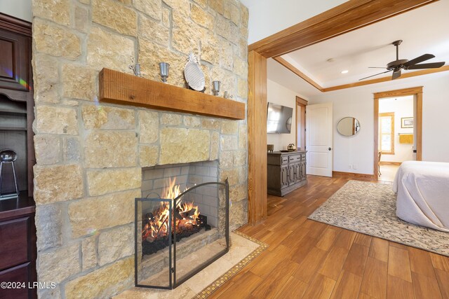 bedroom featuring a raised ceiling, a stone fireplace, wood finished floors, and baseboards