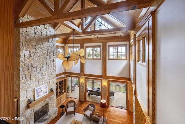 living area featuring baseboards, wood finished floors, a stone fireplace, high vaulted ceiling, and beam ceiling