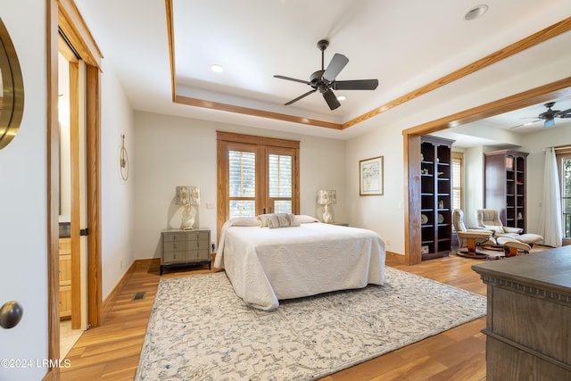 bedroom featuring light wood-style floors, a raised ceiling, ceiling fan, and baseboards