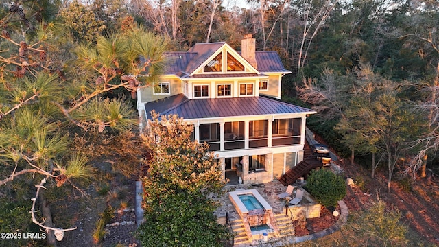 exterior space featuring a sunroom, a chimney, metal roof, a standing seam roof, and a patio area