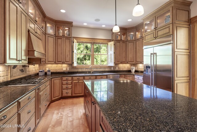 kitchen featuring decorative backsplash, brown cabinets, stainless steel appliances, ventilation hood, and a sink