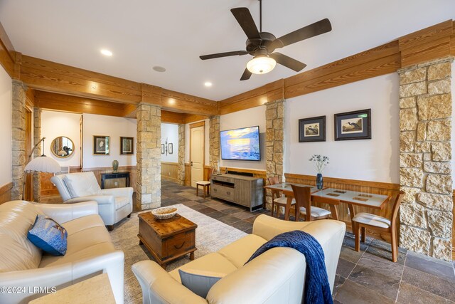 living area featuring decorative columns, stone tile floors, a ceiling fan, a wainscoted wall, and recessed lighting