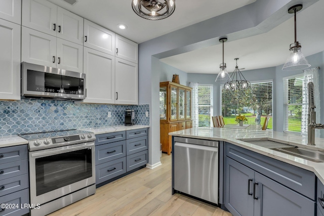 kitchen with appliances with stainless steel finishes, white cabinetry, backsplash, hanging light fixtures, and light hardwood / wood-style flooring