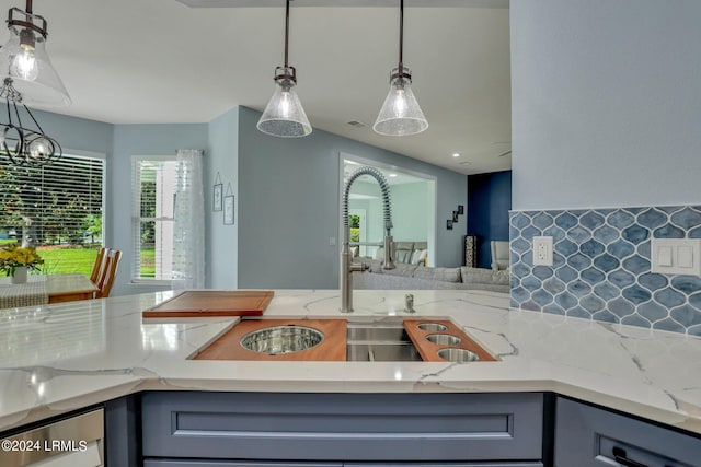 kitchen featuring light stone counters, hanging light fixtures, and gray cabinetry