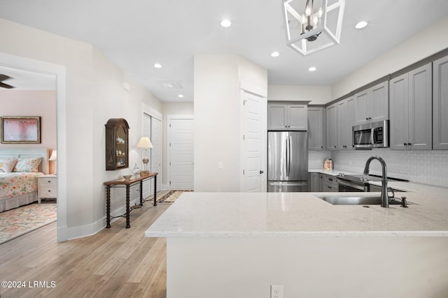 kitchen featuring sink, backsplash, kitchen peninsula, stainless steel appliances, and light wood-type flooring