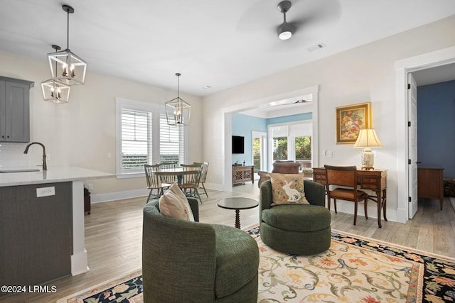 living room with sink, ceiling fan with notable chandelier, and light hardwood / wood-style flooring