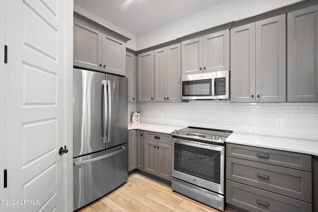 kitchen featuring appliances with stainless steel finishes, gray cabinetry, backsplash, and light hardwood / wood-style floors