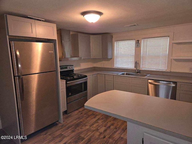 kitchen with appliances with stainless steel finishes, dark hardwood / wood-style floors, sink, a textured ceiling, and wall chimney exhaust hood