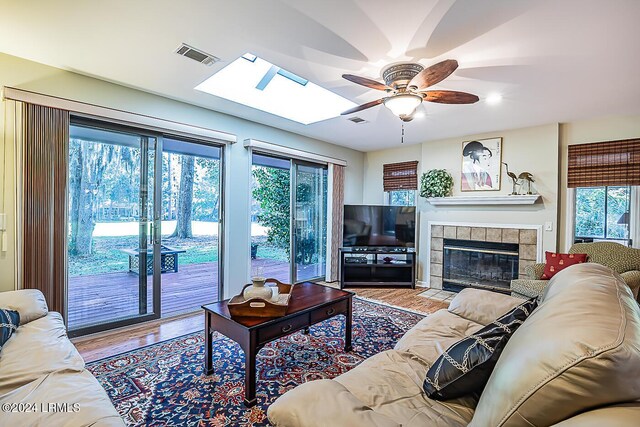 living room with a tiled fireplace, ceiling fan, a wealth of natural light, and light wood-type flooring