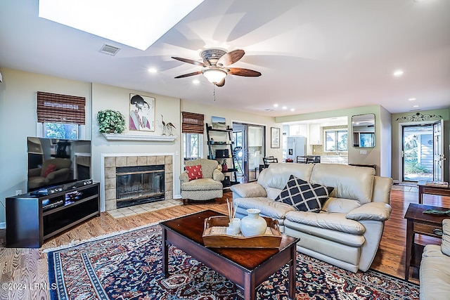 living room featuring a tiled fireplace, ceiling fan, and light wood-type flooring