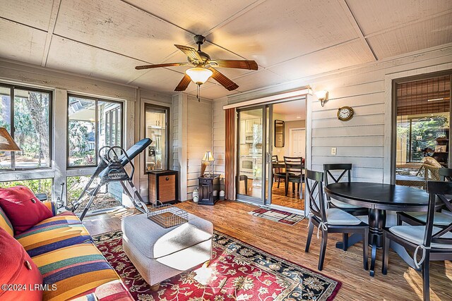 living room with wood-type flooring, ceiling fan, and wood walls