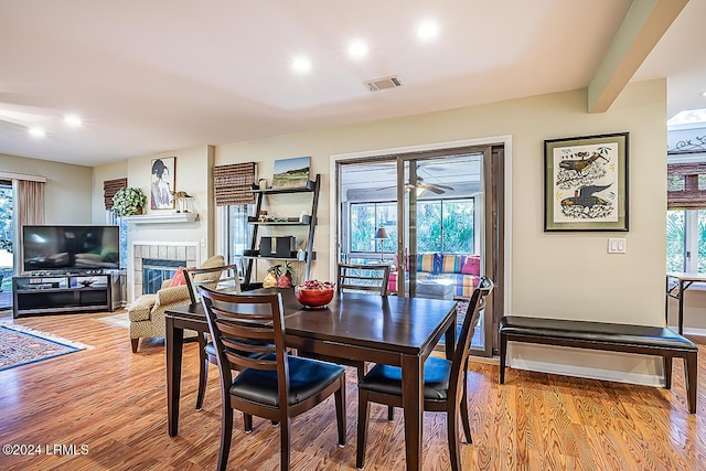 dining room with beamed ceiling, a wealth of natural light, a fireplace, and light wood-type flooring