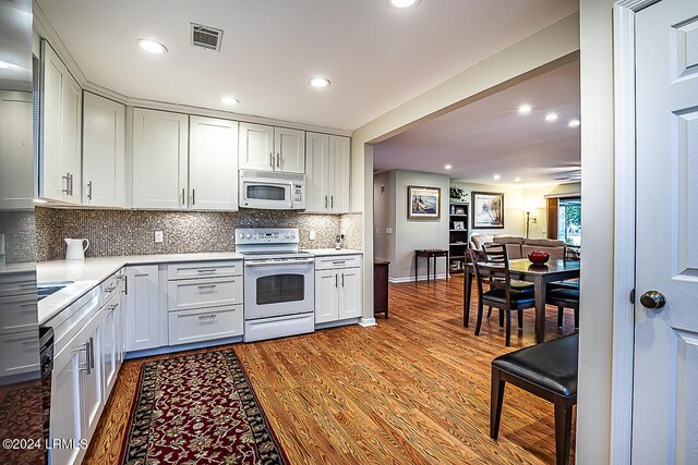 kitchen with white cabinetry, backsplash, white appliances, and light hardwood / wood-style floors