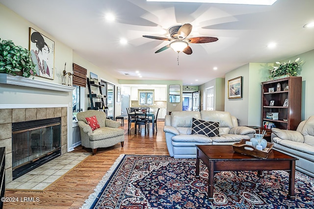 living room with light hardwood / wood-style flooring, a tile fireplace, and ceiling fan