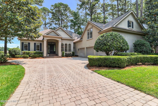 45 Manchester Ct, Bluffton, SC 29910 - view of front of home featuring decorative driveway, stucco siding, a chimney, an attached garage, and a front lawn