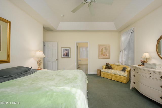 bedroom featuring a raised ceiling, dark carpet, connected bathroom, and ceiling fan